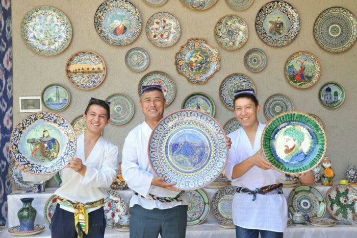 Three men holding decorative plates against a wall of ceramic plates