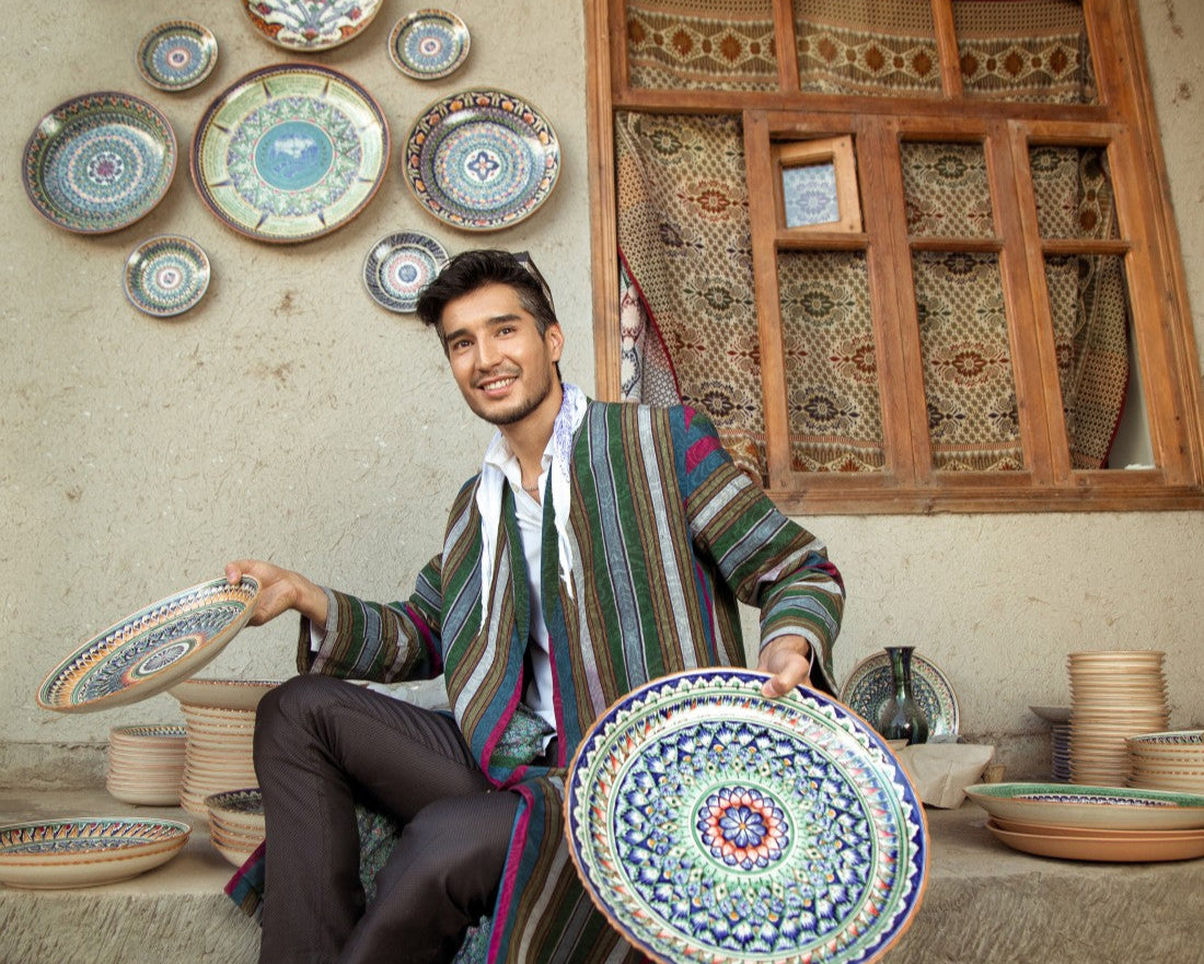 Man holding a decorative plate in a room with ceramic plates and vases on the wall.