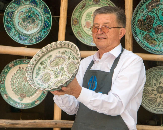 Man holding a decorative plate with more plates displayed on a wall behind him